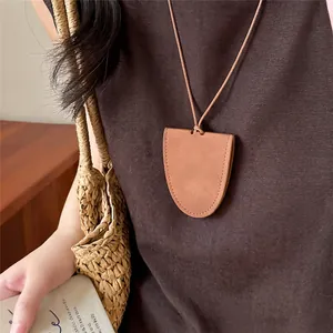 Detailopname van een minimalistische bruine leren hanger ketting op een donkerbruine top