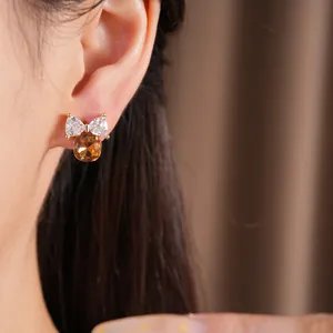 Close-up detail van een 14k vergulde strikoorbel met amberkleurige zirkonia op het oor.