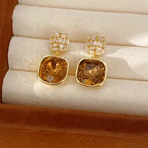 Macrodetail van vierkante gouden oorbellen met honingamberkleurige kristallen en zirkonia