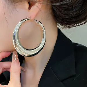 Detailopname van extra grote zilveren metalen oorringen gedragen door een model in blazer.