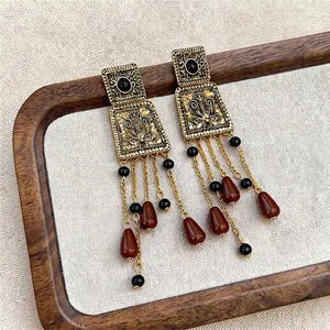 Vintage palace style square tassel earrings with red-brown beads on a wooden tray