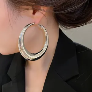 Close-up van oversized gepolijste zilveren oorringen op een model in een zwarte blazer