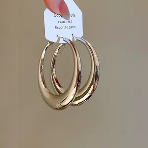Detailopname van grote goudkleurige oorringen met een gladde spiegelende afwerking.