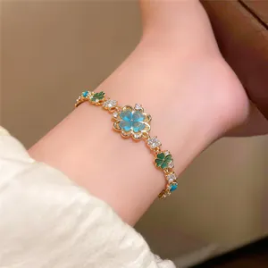 Detail shot of a delicate gold-toned bracelet with blue and green zircon flower charms.