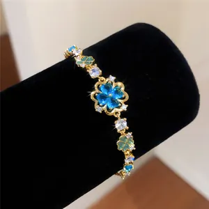 Close-up of a golden flower bracelet featuring blue heart-shaped zircon clover charms.