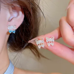 Close-up of sparkling zircon bow stud earrings shown on ear and held in hand.
