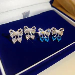 Detailed view of silver bow knot earrings with white and blue heart-shaped zircons