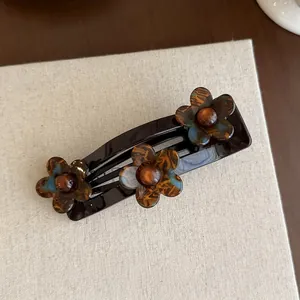 Detailopname van haarklem met schildpad acryl bloemen en amberkleurige kralen