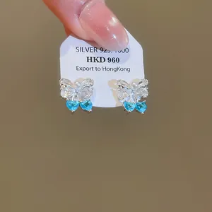 Close-up of elegant bowknot stud earrings featuring blue heart stones and a pearl accent
