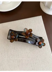 Macro-opname van een acrylbloem met vintage schildpadmotief op een donkere haarclip