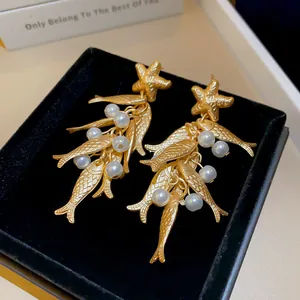 Macro view of vintage gold ocean style earrings with starfish, fish charms and pearls