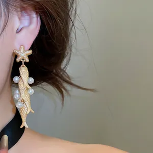 Close-up of vintage ocean-themed earrings with starfish, golden fish, and pearls