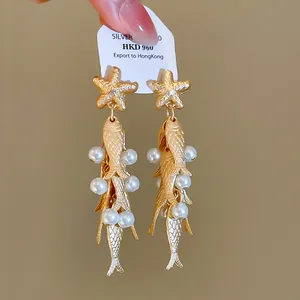 Detailed macro view of vintage ocean style gold starfish and fish drop earrings with white pearls