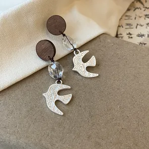 Macro view of vintage swallow drop earrings featuring wooden studs and clear crystal beads
