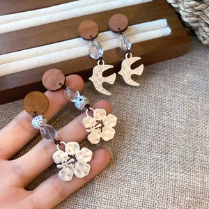 Detailed view of vintage bird and flower pendant earrings with wooden studs and clear beads.