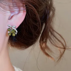 Sparkling silver bow earrings featuring zircon stones and green grape beads on ear.