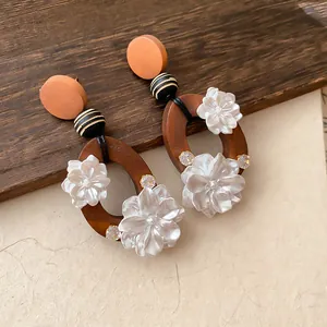 Detailaufnahme von Vintage-Holzohrringen mit weißen Acrylblumen und Strasssteinen.