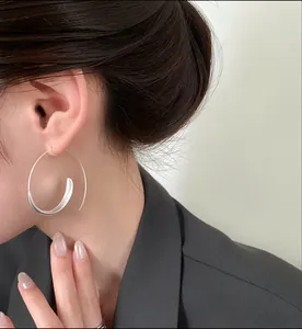 Macro view of a stylish minimalist silver spiral hoop earring worn on a female model's ear.
