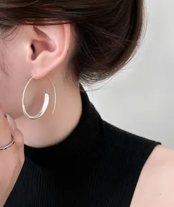 Detailed macro view of a minimalist silver spiral hoop earring worn on a female ear