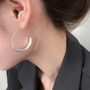 Close-up detail of an oversized minimalist silver spiral hoop earring worn by a model