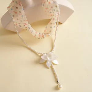 Elegant detailed view of white resin flower pendant on pearl necklace with polka dot chiffon ribbon