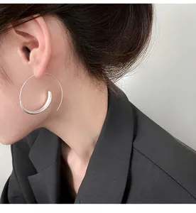 Close-up detail of a minimalist silver spiral hoop earring worn on a model's ear.