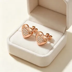 Gros plan sur des boucles d'oreilles cœur en or rose avec cristaux dans un écrin beige