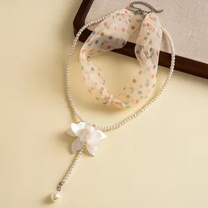 Close-up detail view of elegant pearl necklace with white resin flower and ribbon