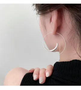 Detail shot of a minimalist silver spiral hoop earring worn by a model with a clean back view