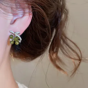Detailweergave van elegante zirkoon strik oorbellen met groene druivenkralen aan het oor