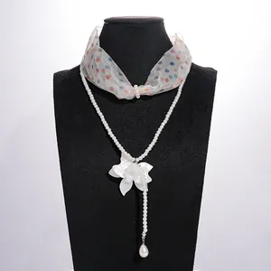 Detail of a double-layer necklace with a resin flower, pearls, and polka dot chiffon scarf.