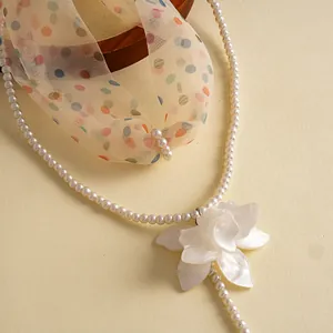Close-up of white resin flower pendant and double-layered pearl necklace.