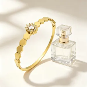 Détail d'un bracelet doré hexagonal avec motif de tournesol à côté d'un parfum.