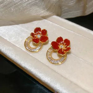 Gros plan des boucles d'oreilles dorées avec fleurs en émail rouge et anneaux en zircone.