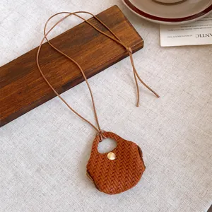 Detailed view of a woven leather bag pendant necklace on a wooden block