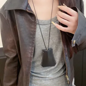 Detail view of a black leather clochette pendant necklace on a long black cord