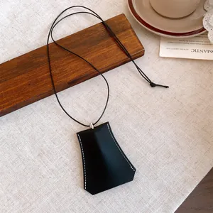 Black leather eyeglass holder pendant necklace on a minimalist wooden lifestyle background