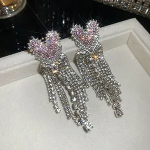 Close-up van roze hartvormige kwastjesoorbellen met fonkelende strass-steentjes.