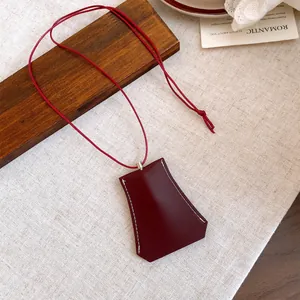 Close-up of a burgundy leather clochette-style pendant on a red cord necklace