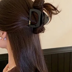 Détail d'une pince à cheveux minimaliste en acrylique noir en forme de D sur cheveux