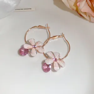 Close-up detail van elegante roségouden oorringen met witte bloembladen en roze zirkoon drop