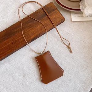 Detailed macro view of a brown leather bag-shaped pendant necklace with white stitching.