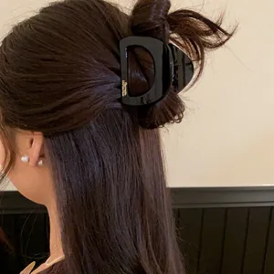 Détail d'une petite pince à cheveux noire en forme de D sur cheveux foncés