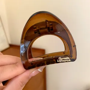 Gros plan sur une petite pince à cheveux en acrylique marron avec logo doré Barrette La France