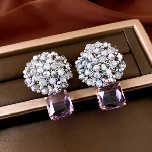 Macro view of beaded zircon earrings with square purple pendant on a jewelry box