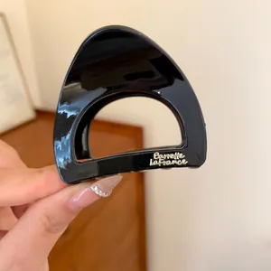 Vue détaillée d'une petite pince à cheveux en acrylique noir avec inscription dorée