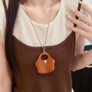 Detail view of a brown woven leather bag pendant necklace worn with a brown dress.
