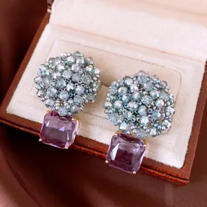 Close-up of elegant beaded earrings with square purple gemstone pendants.