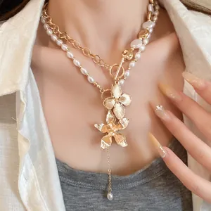 Detailansicht einer geschichteten Perlenkette mit goldenen Blumenanhängern an Model