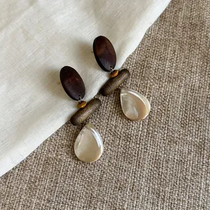 Detailansicht von Vintage-Ohrringen aus Holz und Muschelperlen auf grobem Leinenstoff
